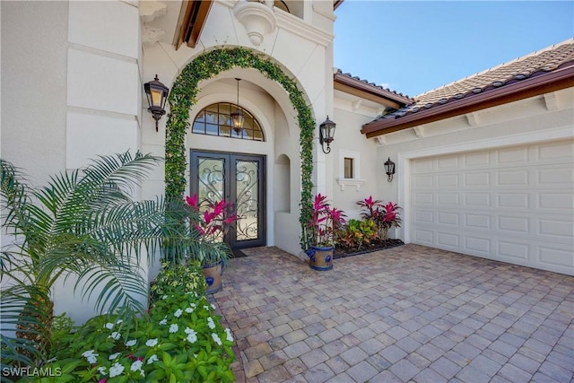 entrance to property featuring a tiled roof, french doors, decorative driveway, and stucco siding