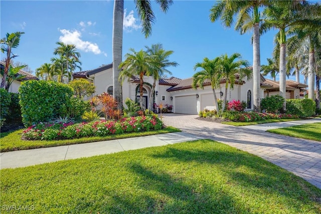 mediterranean / spanish-style house with decorative driveway, stucco siding, a garage, a tiled roof, and a front lawn