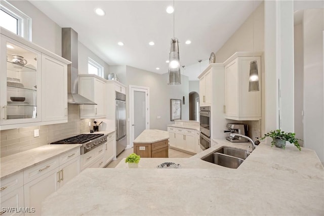 kitchen featuring tasteful backsplash, wall chimney exhaust hood, a kitchen island, appliances with stainless steel finishes, and a sink