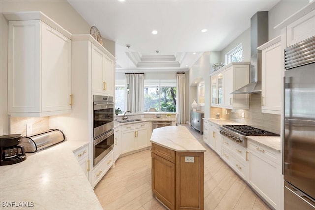 kitchen with tasteful backsplash, appliances with stainless steel finishes, a center island, a tray ceiling, and wall chimney range hood