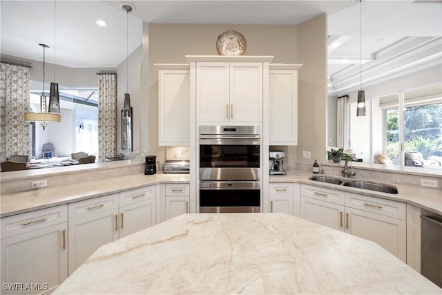 kitchen featuring stainless steel appliances, a sink, white cabinets, hanging light fixtures, and light stone countertops