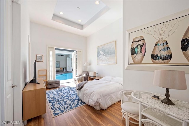 bedroom with access to outside, a raised ceiling, wood finished floors, and recessed lighting