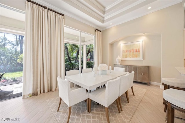 dining space with a raised ceiling, crown molding, light wood-style flooring, and baseboards