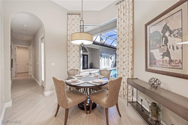 dining space featuring arched walkways, baseboards, a high ceiling, and wood finished floors