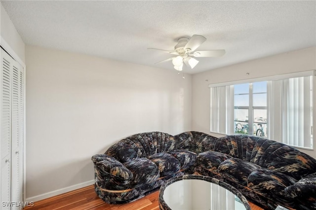 living area featuring a ceiling fan, a textured ceiling, baseboards, and wood finished floors