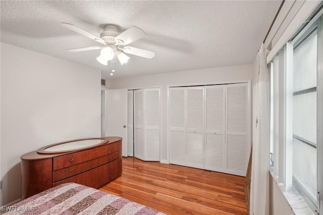 bedroom featuring multiple closets, visible vents, light wood-style flooring, a ceiling fan, and a textured ceiling