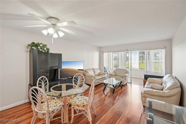 living area with a ceiling fan, a textured ceiling, baseboards, and wood finished floors