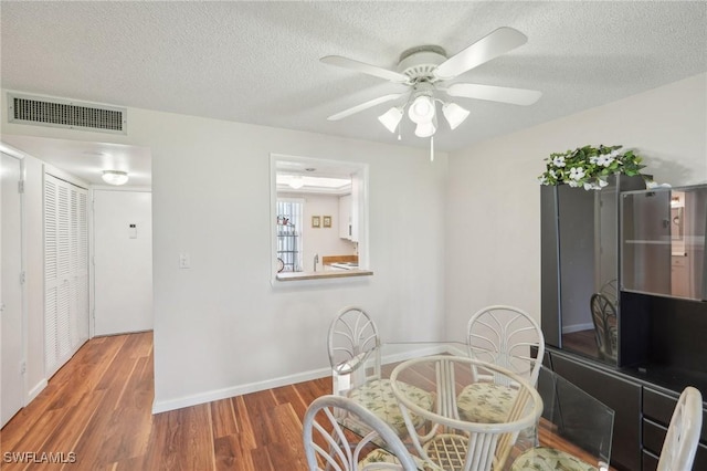 dining room featuring a textured ceiling, wood finished floors, visible vents, baseboards, and a ceiling fan