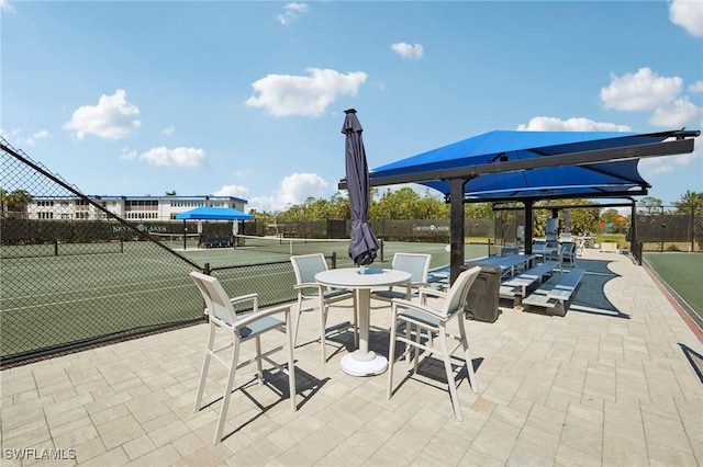 view of patio featuring a tennis court and fence