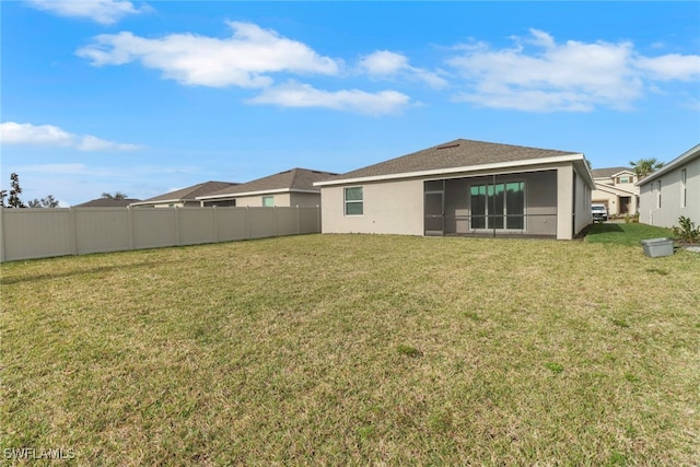 rear view of property with stucco siding, a yard, and fence