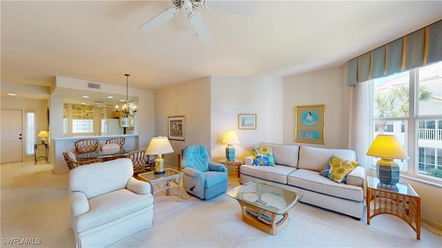 carpeted living area featuring a wealth of natural light, visible vents, and ceiling fan with notable chandelier