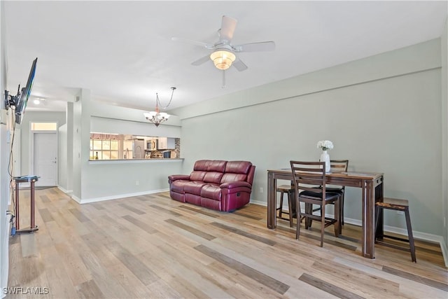 living area featuring ceiling fan with notable chandelier, baseboards, and wood finished floors