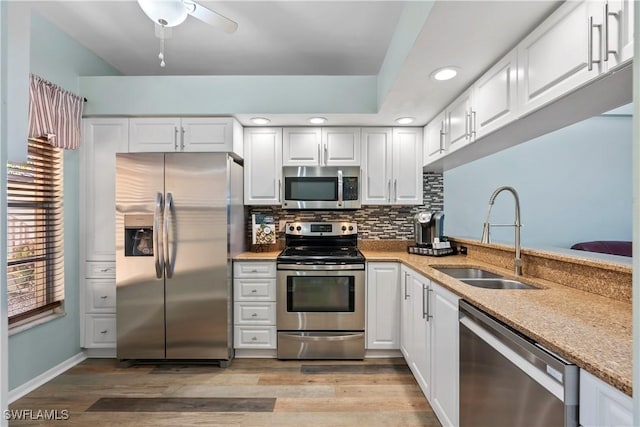 kitchen featuring white cabinets, a sink, stainless steel appliances, light wood-style floors, and backsplash