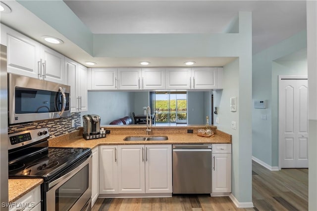 kitchen featuring tasteful backsplash, white cabinets, light wood-style flooring, stainless steel appliances, and a sink