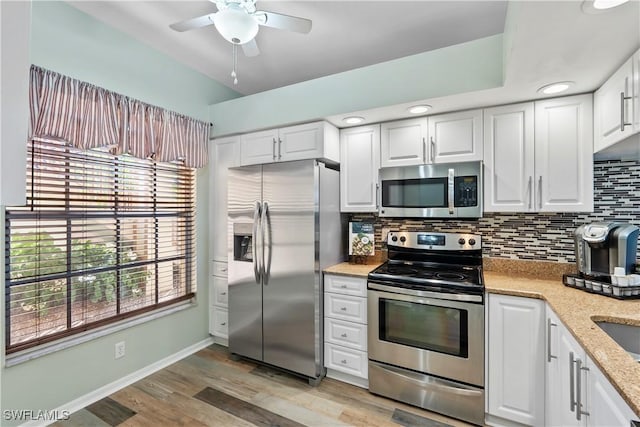 kitchen featuring light wood finished floors, tasteful backsplash, appliances with stainless steel finishes, white cabinets, and ceiling fan