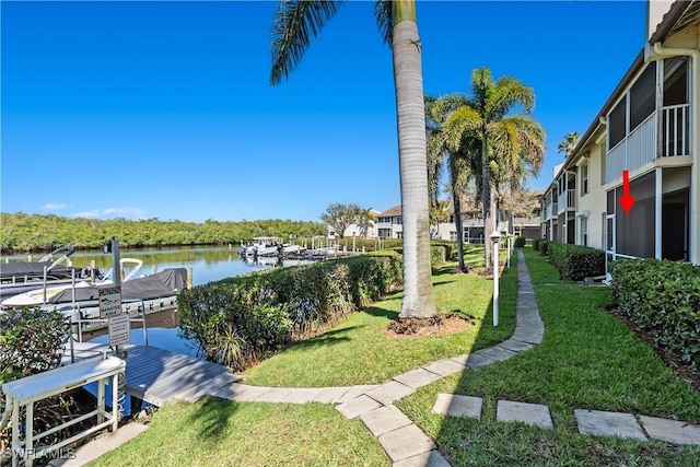 surrounding community with a boat dock, a water view, and a lawn