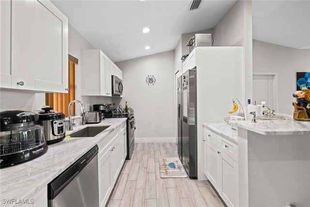 kitchen with stainless steel appliances, wood finish floors, a sink, white cabinetry, and light stone countertops