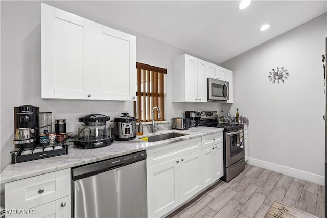 kitchen with light stone counters, wood finish floors, a sink, white cabinetry, and appliances with stainless steel finishes