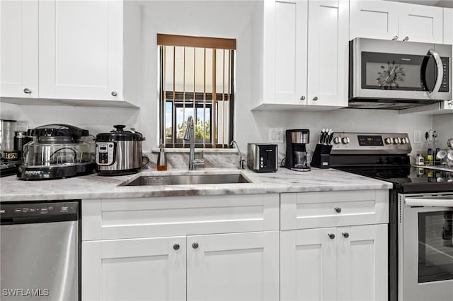 kitchen with white cabinets, light stone counters, stainless steel appliances, and a sink