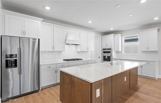 17333 Leaning Oak Trl, North Fort Myers, FL 33917 - kitchen featuring appliances with stainless steel finishes, premium range hood, light wood finished floors, white cabinetry, and a kitchen island with sink