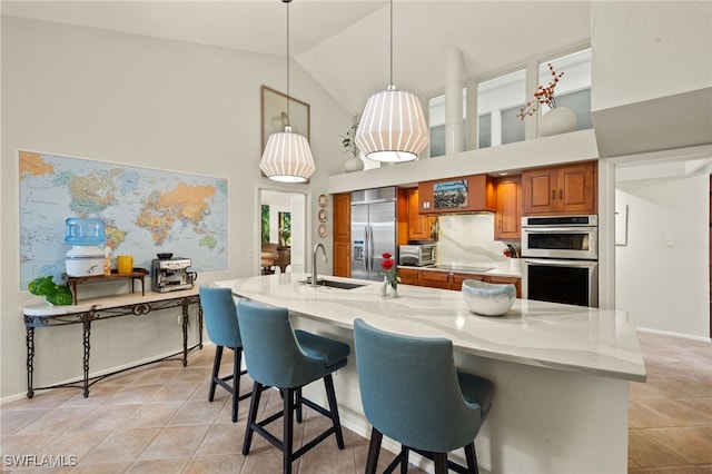 kitchen featuring light stone counters, decorative light fixtures, stainless steel appliances, brown cabinetry, and a sink