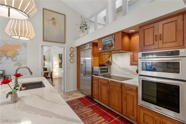 kitchen featuring appliances with stainless steel finishes, pendant lighting, brown cabinetry, and a sink