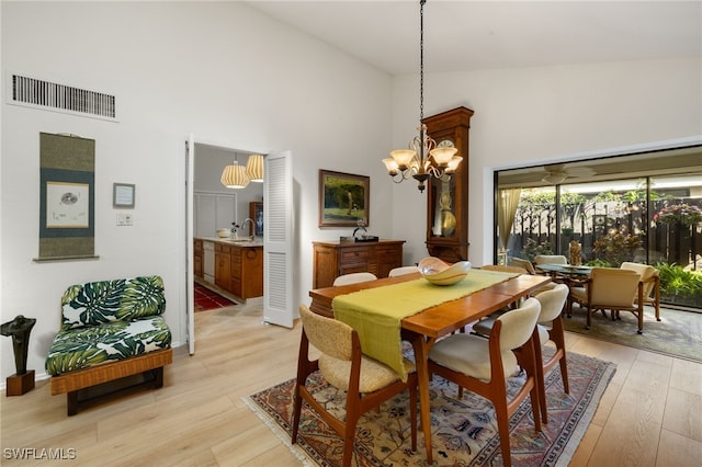 dining area with high vaulted ceiling, light wood finished floors, visible vents, and an inviting chandelier