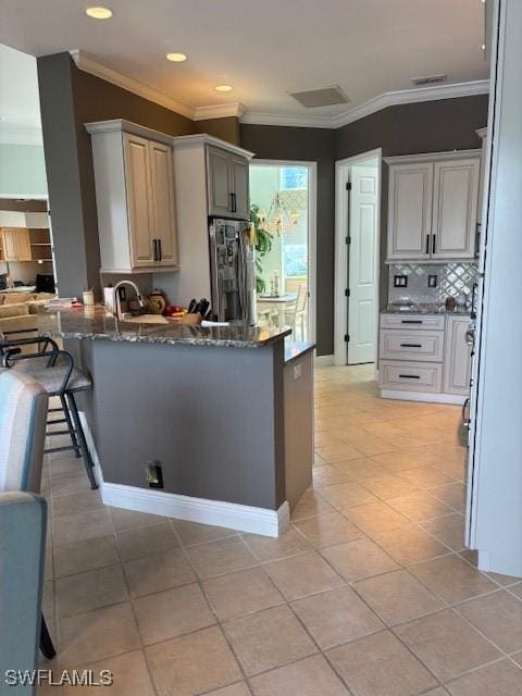 kitchen featuring dark stone countertops, a peninsula, crown molding, and stainless steel fridge with ice dispenser