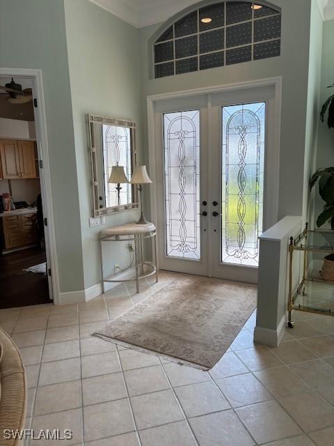 tiled entrance foyer with crown molding, french doors, baseboards, and a towering ceiling