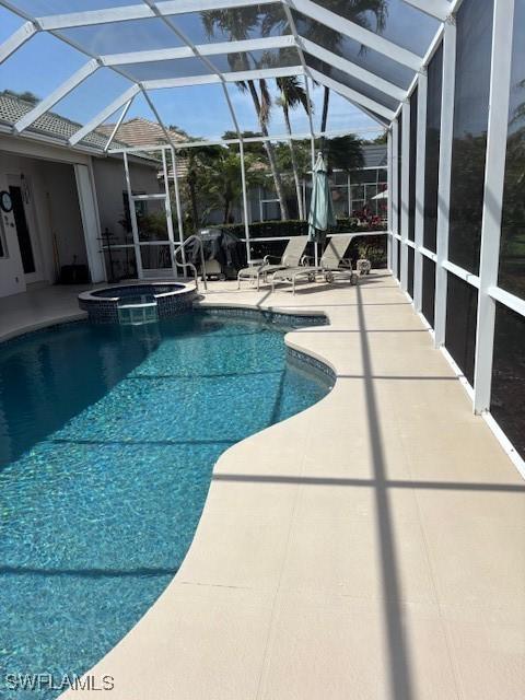 view of pool with glass enclosure, a pool with connected hot tub, and a patio area