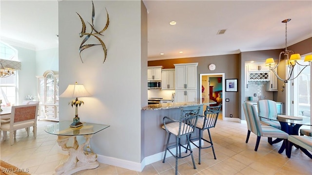 kitchen with stainless steel microwave, light stone counters, a notable chandelier, and crown molding