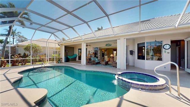 view of swimming pool featuring glass enclosure, a patio area, a pool with connected hot tub, and a ceiling fan