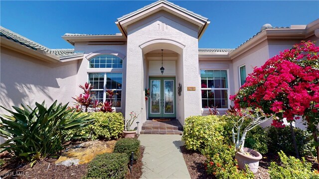 property entrance with a tiled roof, french doors, and stucco siding