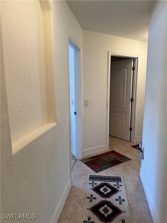 hall featuring light tile patterned flooring and baseboards