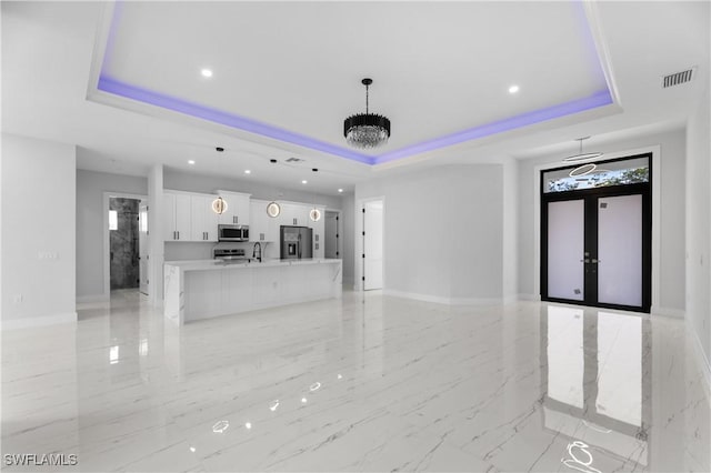 unfurnished living room with visible vents, a tray ceiling, and french doors