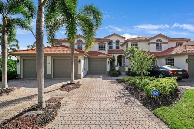 mediterranean / spanish home featuring a tiled roof, decorative driveway, an attached garage, and stucco siding