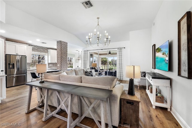 living room with baseboards, visible vents, lofted ceiling, wood finished floors, and a chandelier