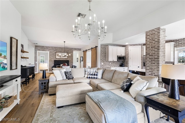 living area featuring a barn door, a notable chandelier, brick wall, visible vents, and light wood finished floors