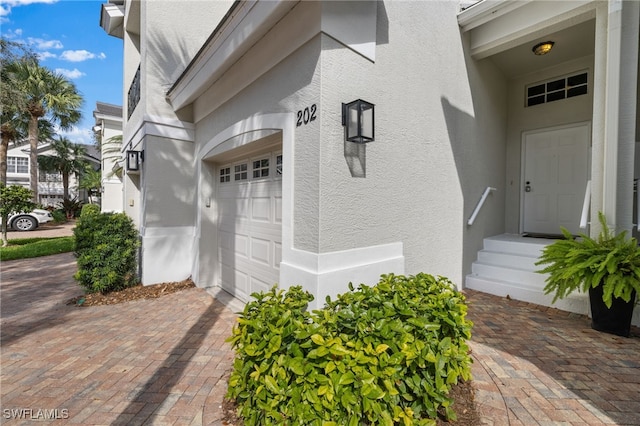 view of exterior entry with a garage, decorative driveway, and stucco siding