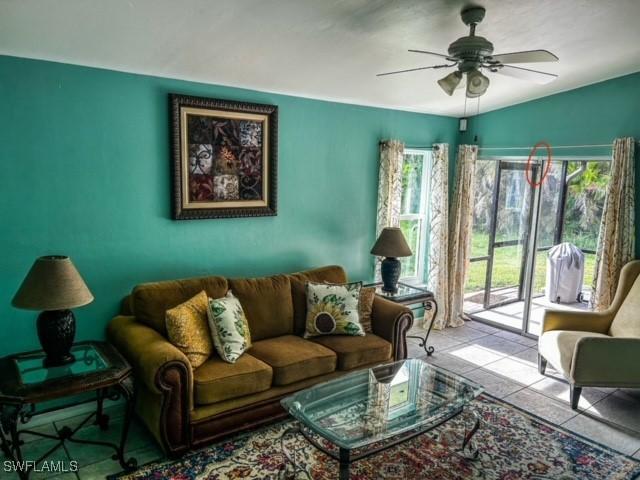 living area featuring lofted ceiling, light tile patterned floors, plenty of natural light, and a ceiling fan