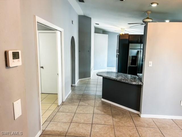 kitchen featuring dark countertops, light tile patterned flooring, fridge with ice dispenser, and ceiling fan