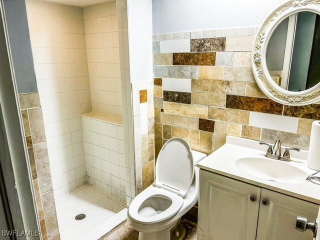 bathroom featuring toilet, a stall shower, tile walls, and vanity