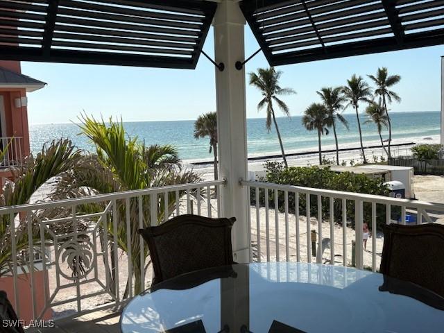 balcony featuring a view of the beach, a water view, a pergola, and outdoor dining space