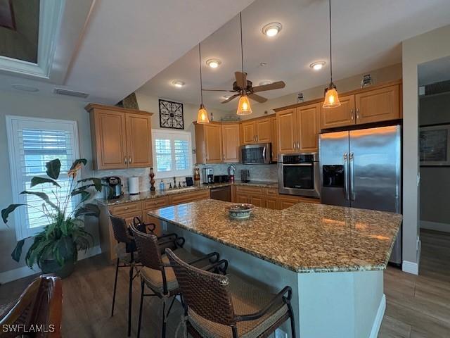 kitchen with a center island, a kitchen bar, stone countertops, ceiling fan, and appliances with stainless steel finishes