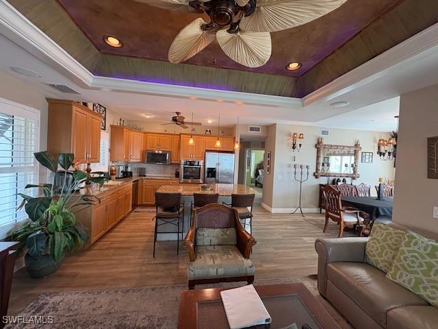living area with a ceiling fan, a raised ceiling, and light wood-type flooring