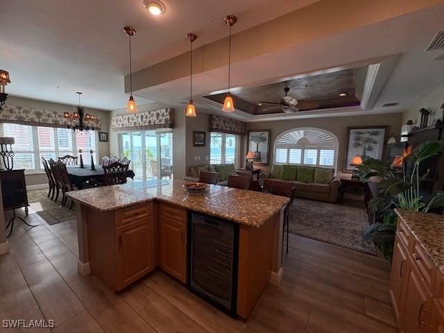 kitchen with ceiling fan with notable chandelier, wood finished floors, wine cooler, a wealth of natural light, and a tray ceiling