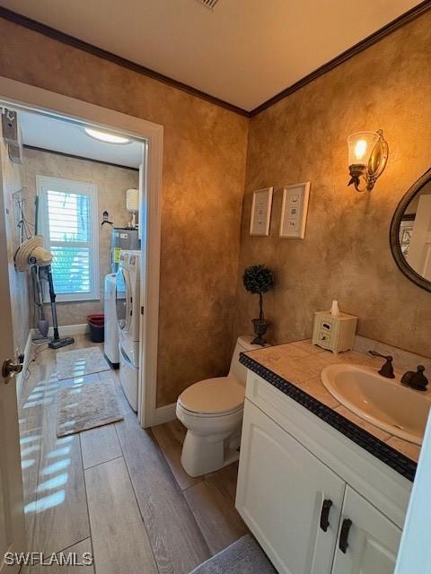 full bathroom featuring toilet, wood finished floors, vanity, ornamental molding, and washing machine and clothes dryer