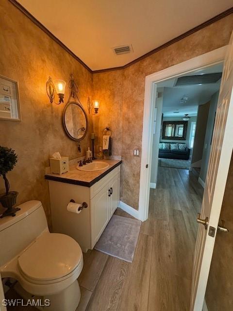 bathroom with toilet, ornamental molding, visible vents, vanity, and wood finished floors