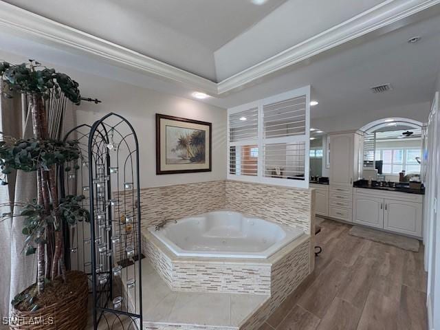 full bathroom with a garden tub, a tray ceiling, visible vents, vanity, and ornamental molding