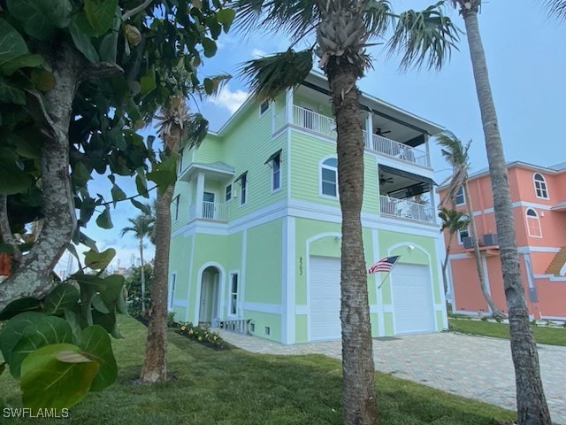 view of property exterior with a balcony, a lawn, decorative driveway, a garage, and stucco siding
